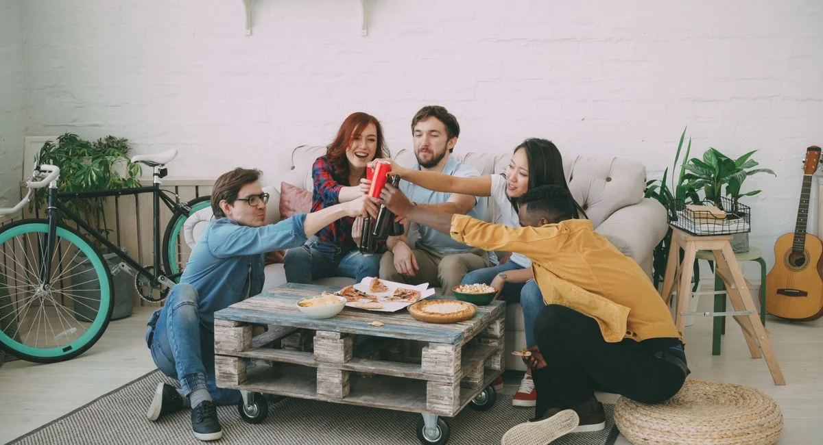 Group of diverse friends sharing pizza and drinks indoors, enjoying a relaxed gathering.