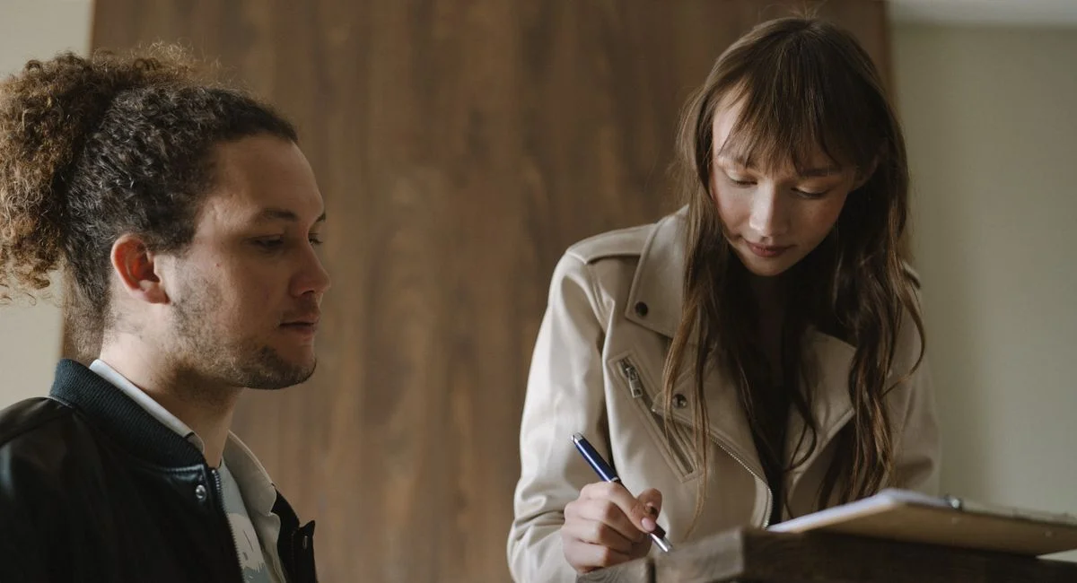 A young couple reviews and signs real estate documents indoors.