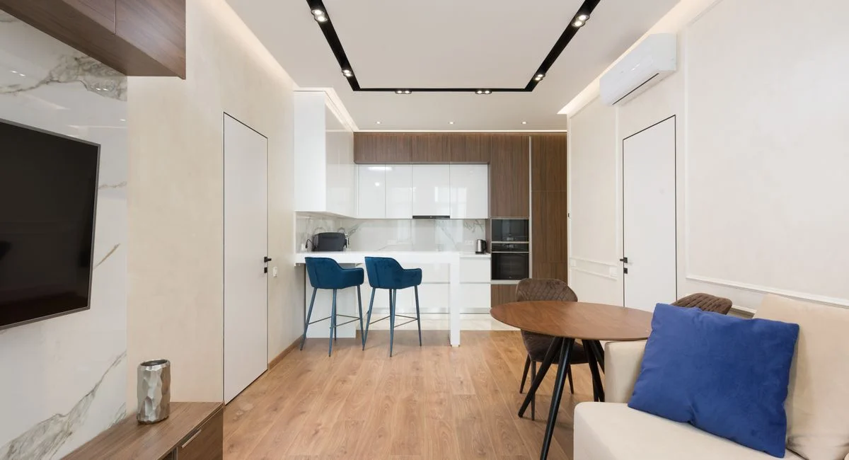 Interior of modern apartment with living room with comfy sofa and wooden furniture near kitchen zone with counter and white c