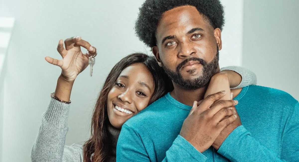 Smiling couple celebrates receiving keys to their new home indoors.