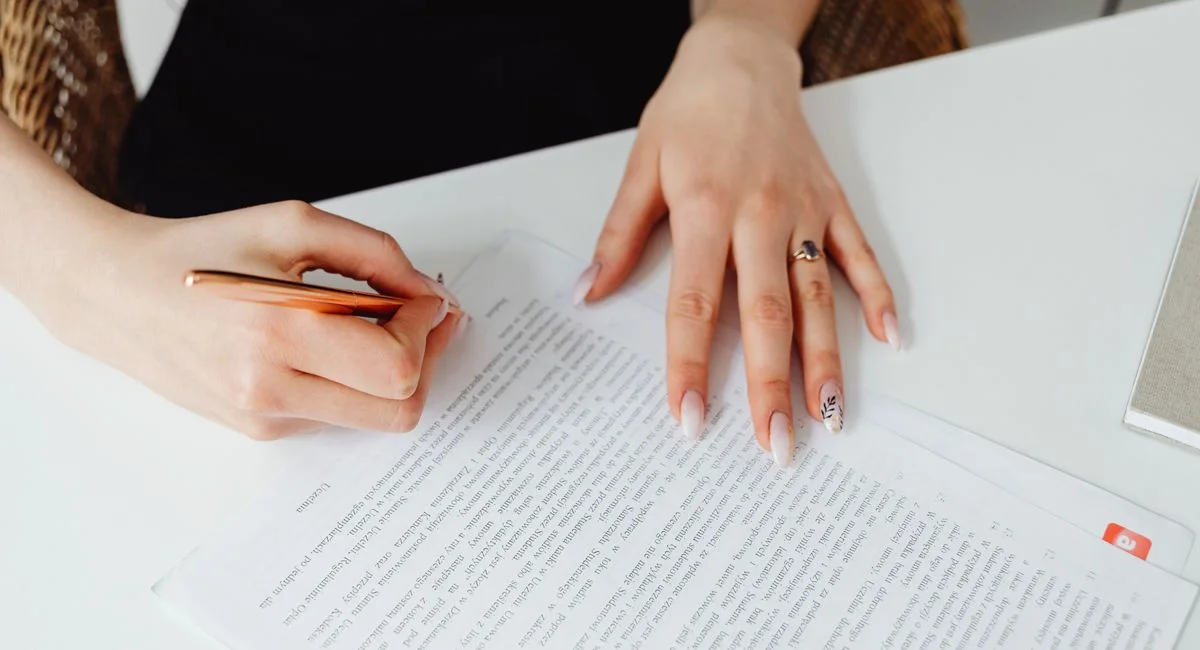A woman signing a document with a pen on a desk, emphasizing hands and writing.