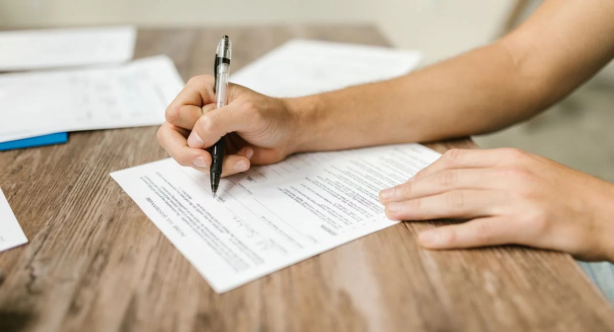 Hand filling out paperwork with a pen, showcasing focus on document completion.