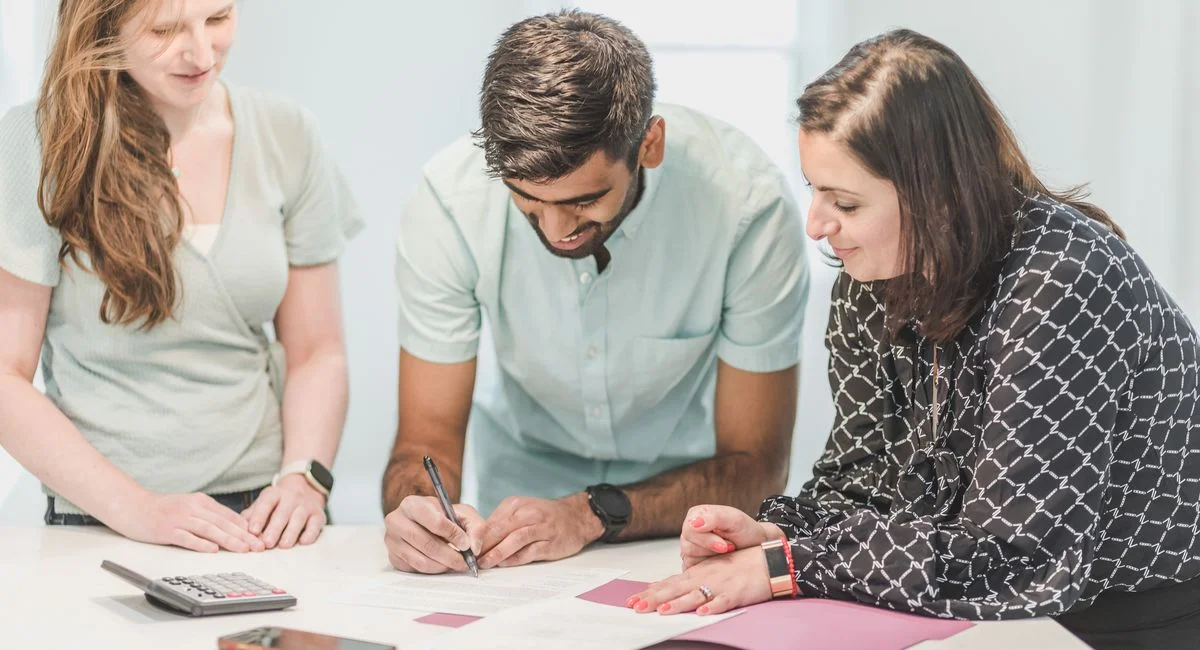 Three adults reviewing and signing real estate documents indoors.