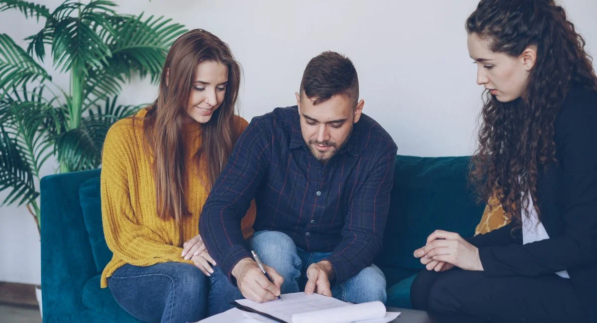 Young couple consults with financial advisor, signing important documents indoors.