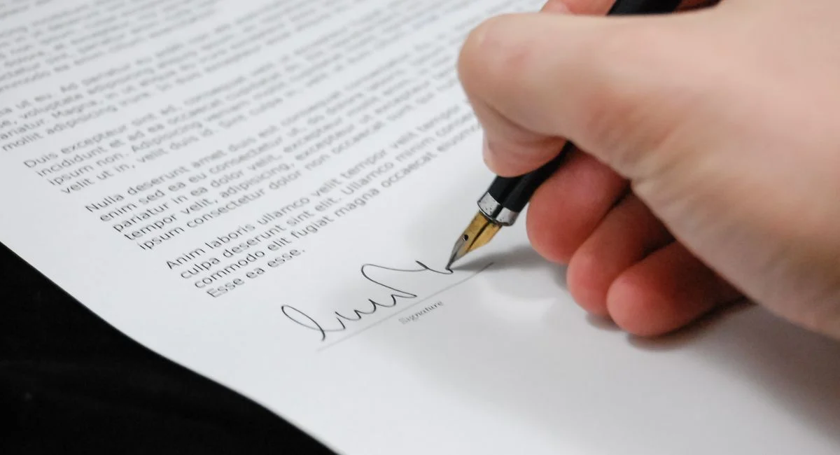 Close-up of a hand signing a legal document with a fountain pen, symbolizing signature and agreement.