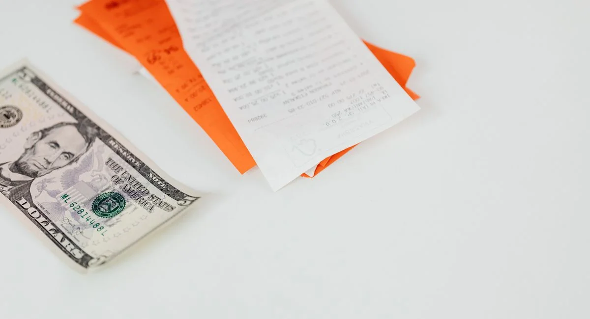 A five dollar bill and receipts on a white surface, emphasizing finance and expenses.