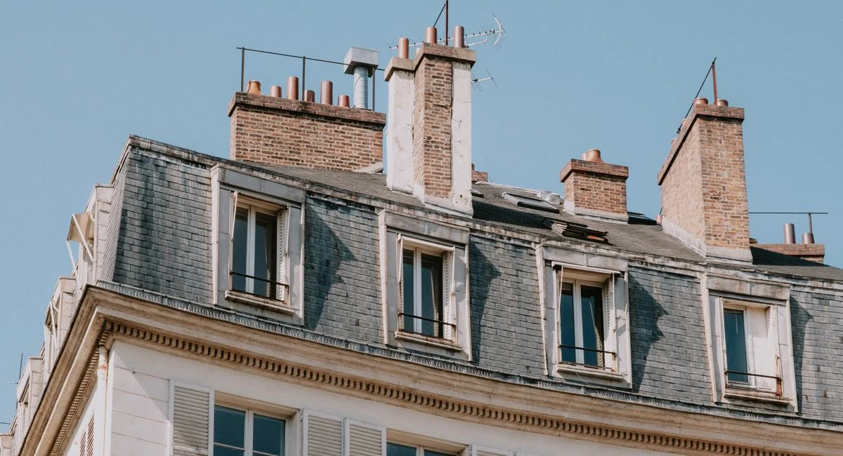 Low-angle view of a classic Parisian apartment building with chimneys and blue sky.