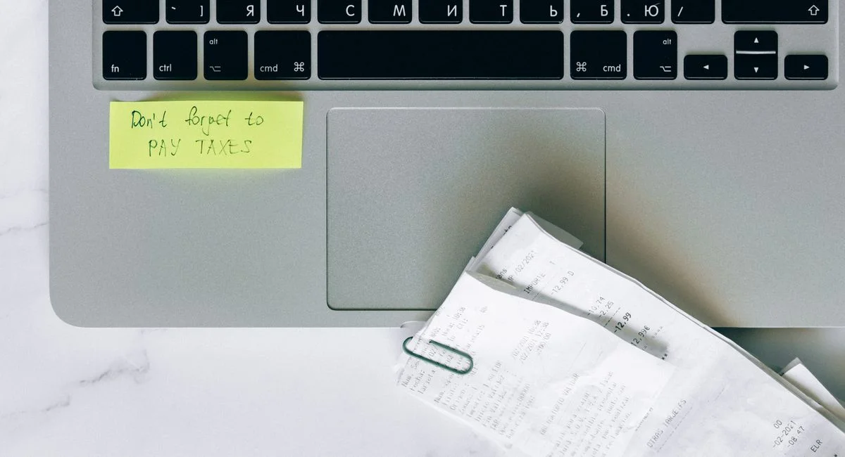 A laptop with a sticky note reminder and receipts, emphasizing tax season organization.