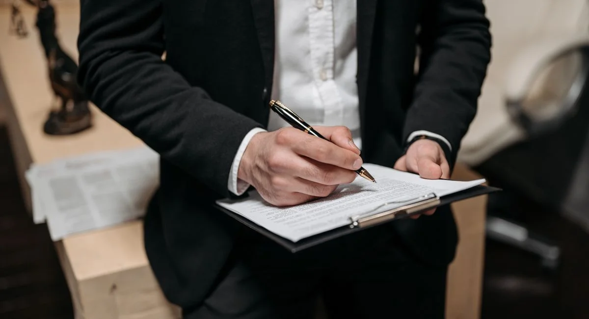 Business professional signing a contract on a clipboard at the office.