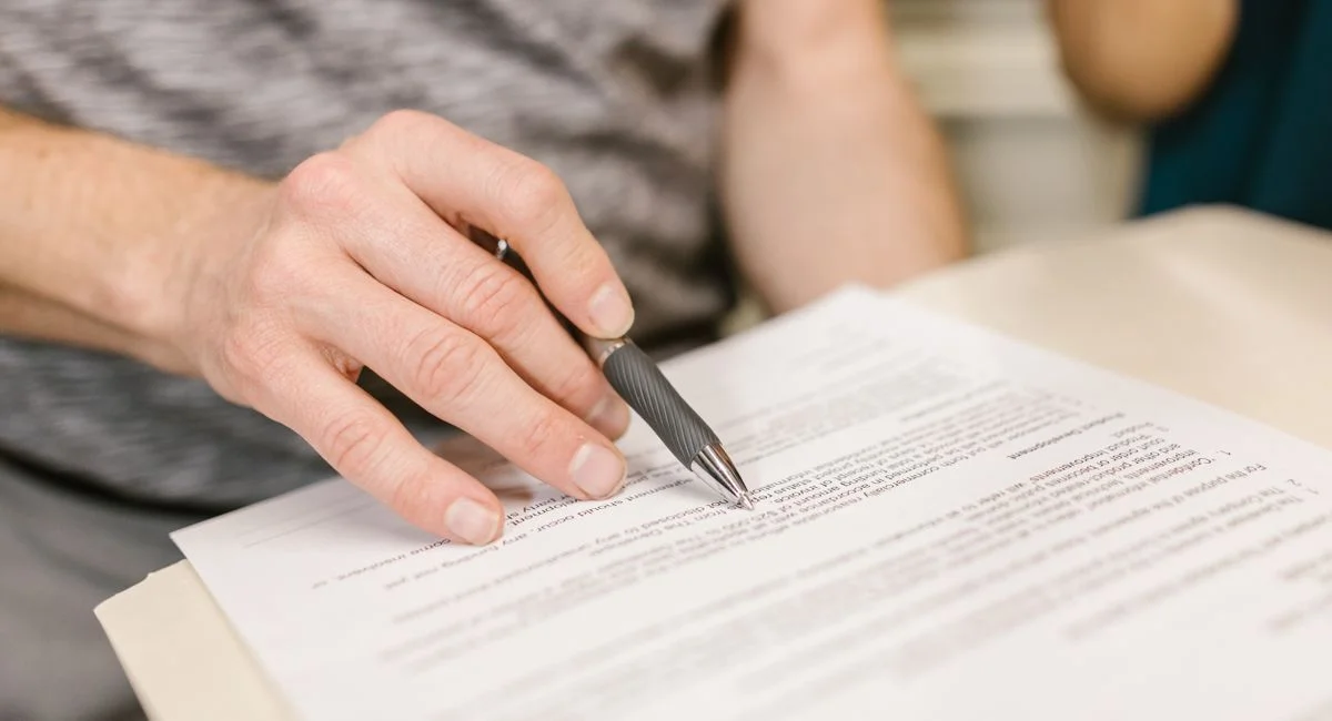 Close-up of a person's hand signing an important legal document with a pen indoors.