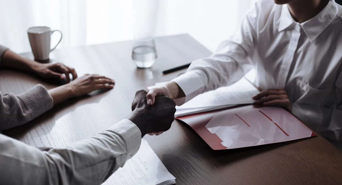 Professional handshake between diverse individuals over a business contract indoors.