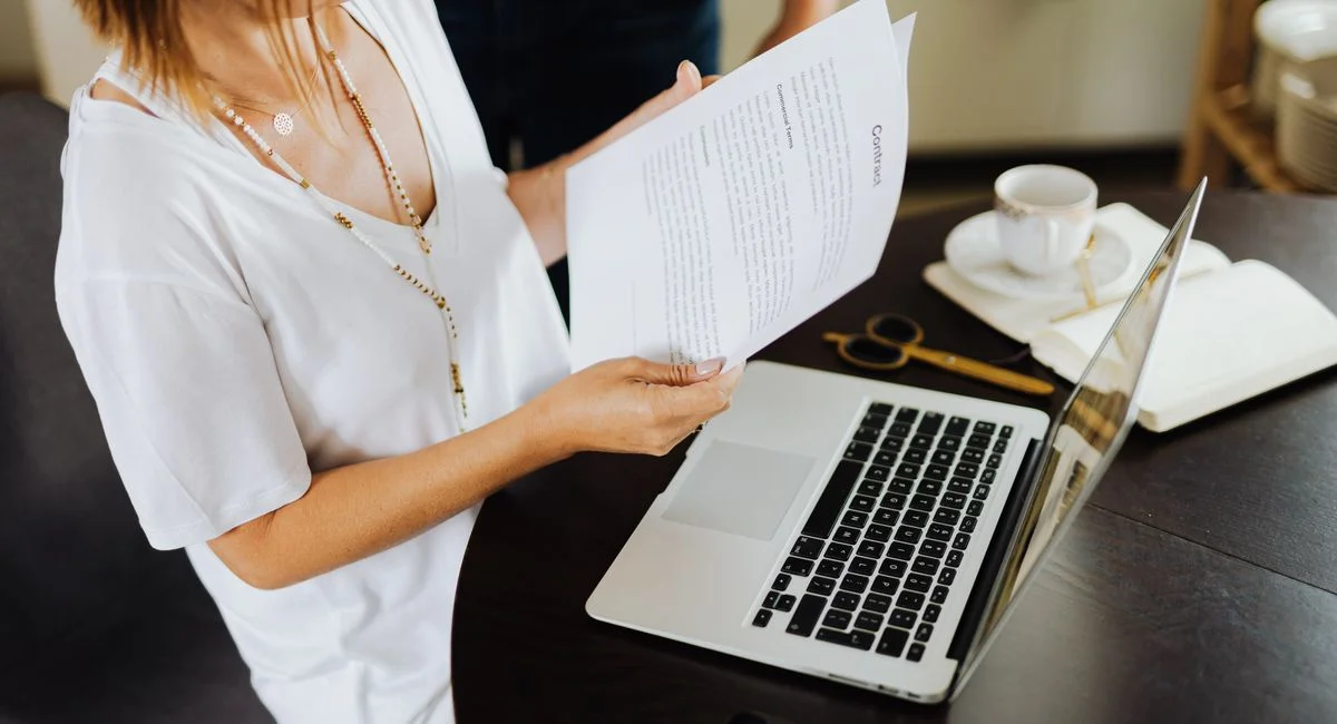 Businesswoman reviewing important documents at her desk with a laptop in a modern office setting.