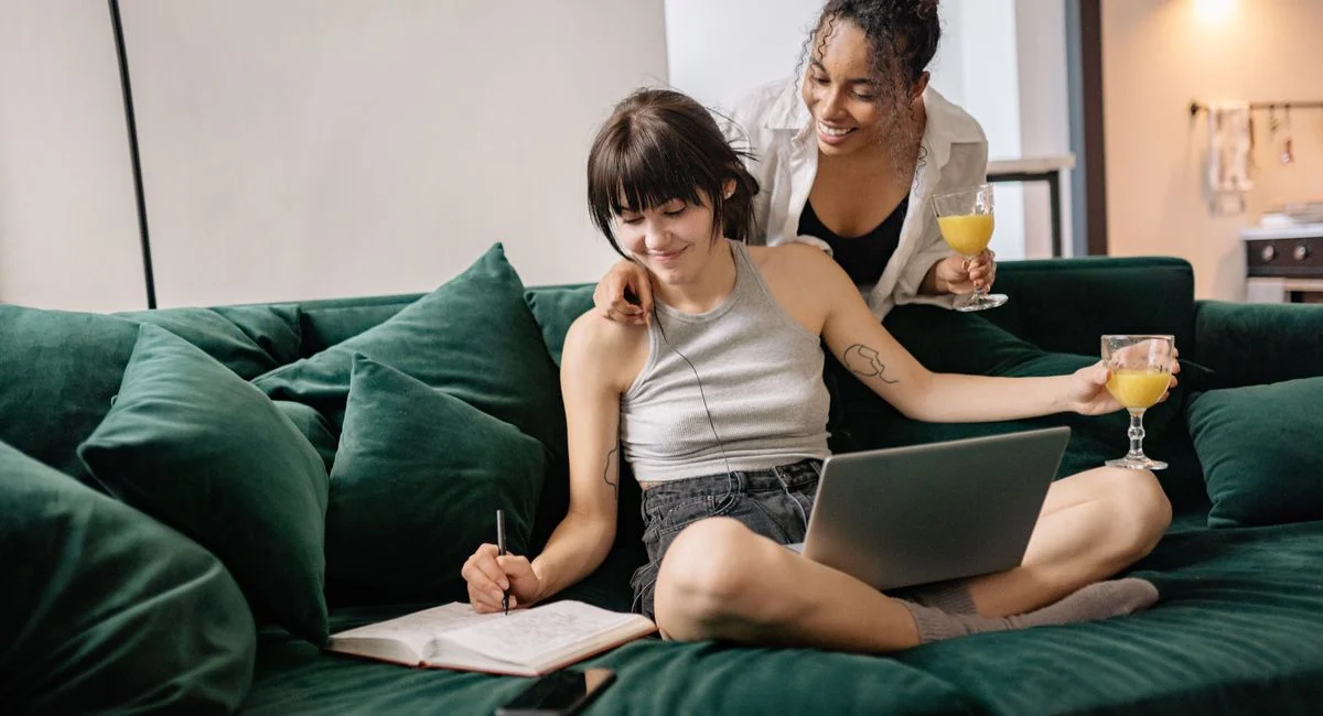 A cheerful same-sex couple enjoying a cozy moment together on a sofa, sipping orange juice.