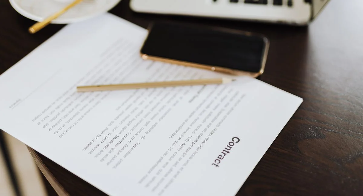 Close-up of a contract with office essentials like a laptop and coffee on a desk.