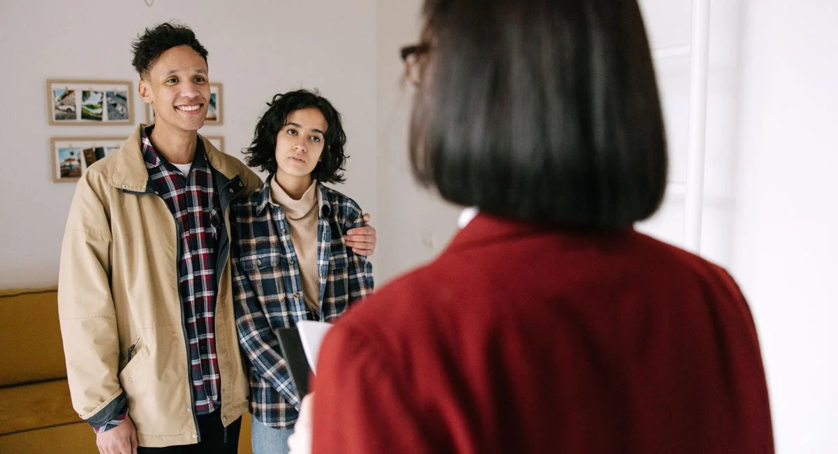 Young couple discussing real estate options with an agent indoors, highlighting home buying process.