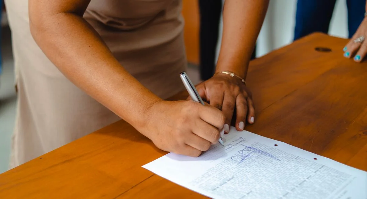 A professional woman signing an official document on a wooden table indoors.