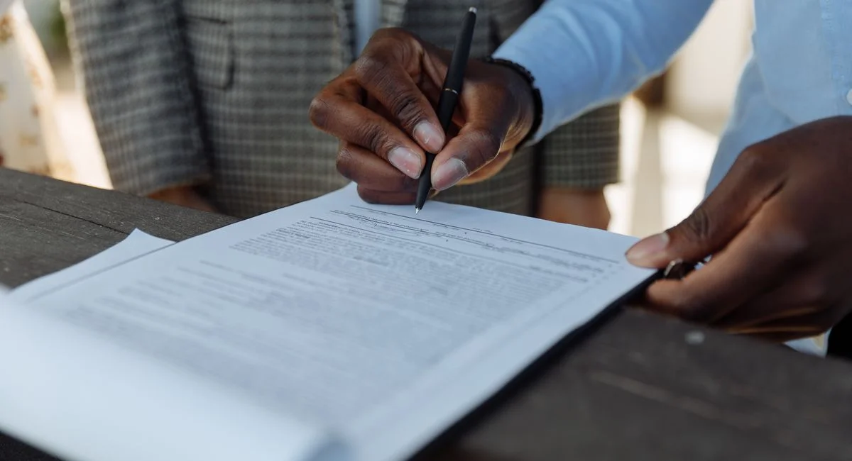 Close-up of business professionals signing a document with a pen indoors.