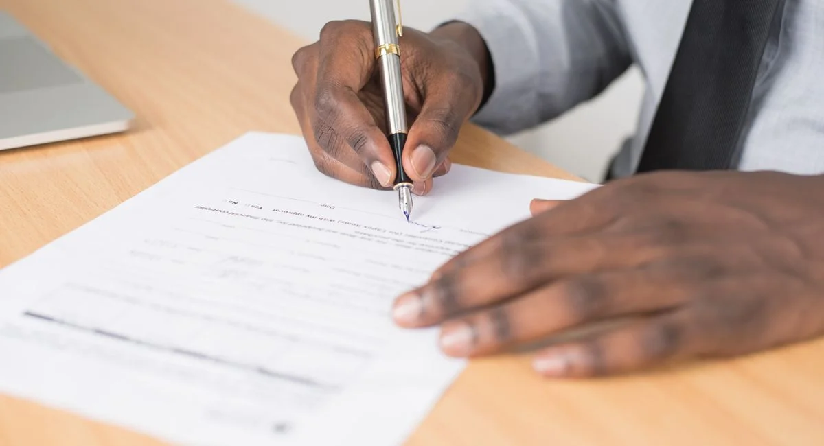 Close-up of a businessman signing a contract at an office desk.