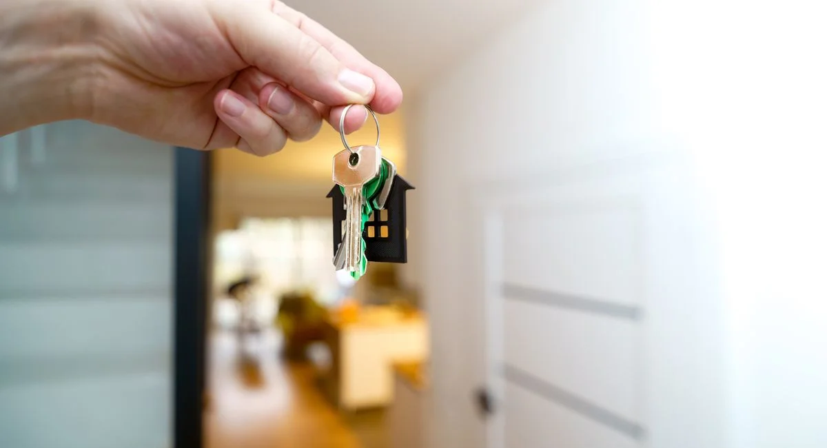 A hand holding house keys inside a modern apartment, symbolizing new property ownership or rental.