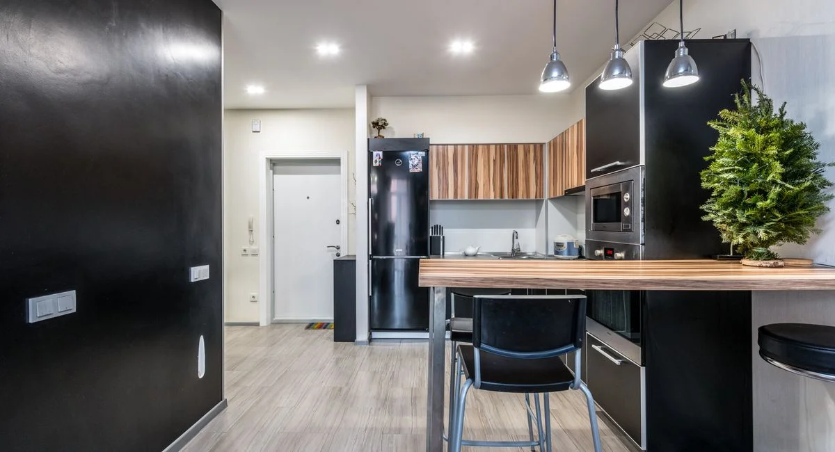 Wooden counter and black cupboards in spacious kitchen with modern appliances and glowing lamps in spacious apartment