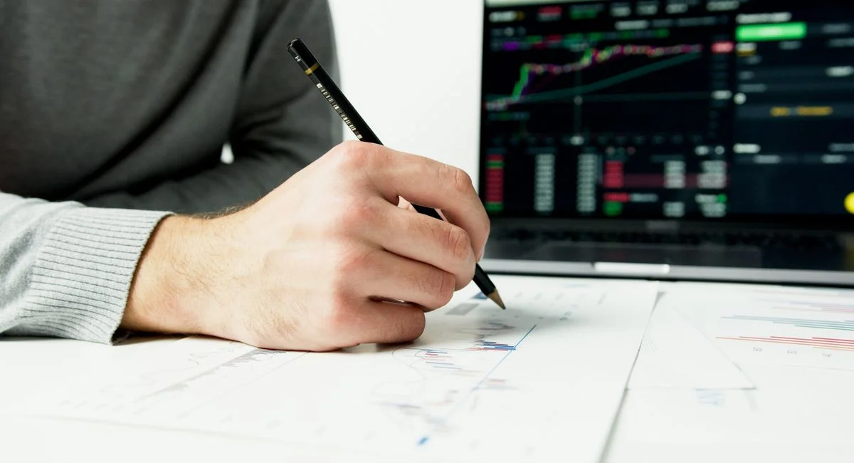 Close-up of a person analyzing financial charts with a laptop displaying stock market data.