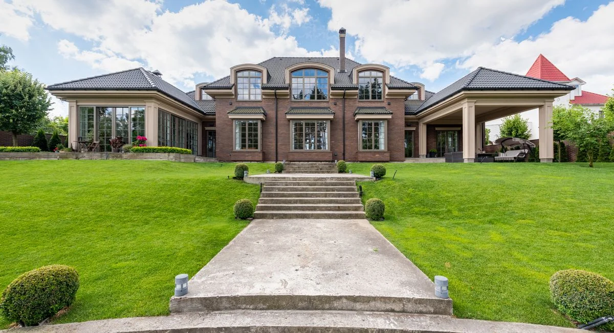 Elegant upscale mansion with lush green garden and clear blue sky.