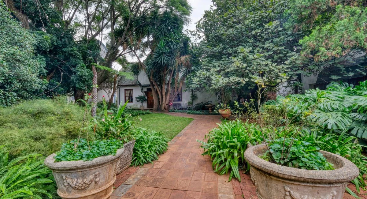 Lush green garden path with potted plants leading to a quaint cottage.