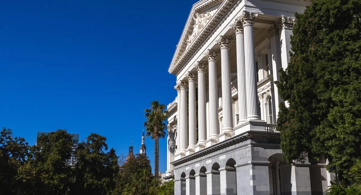 Beautiful sunlit view of the California State Capitol building with classic columns and vibrant blue sky.